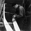 Neg nr 100. Formning av bordspetsens kontur med yxa. Första bordgångens akterhalva om babord. Foto 8.8 (1962).