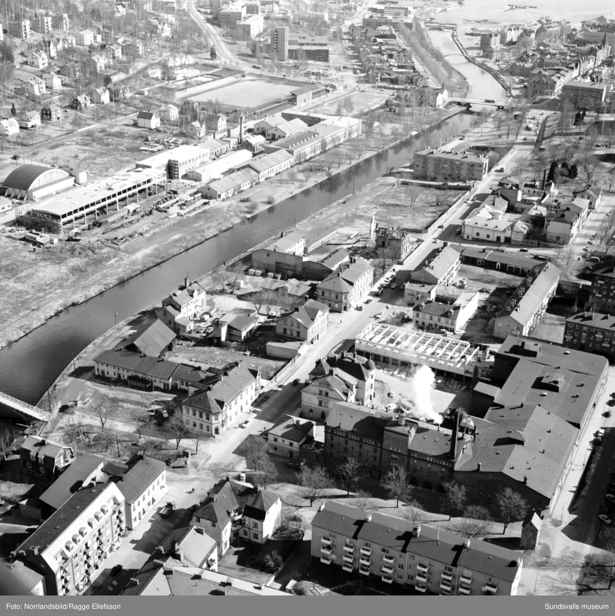 Flygfoto över Storgatan och Selångersån taget från Västra Allén och österut mot Sundsvallsfjärden. Tennishallen, Sundsvalls verkstäder, Idrottsparken och Norrmalm