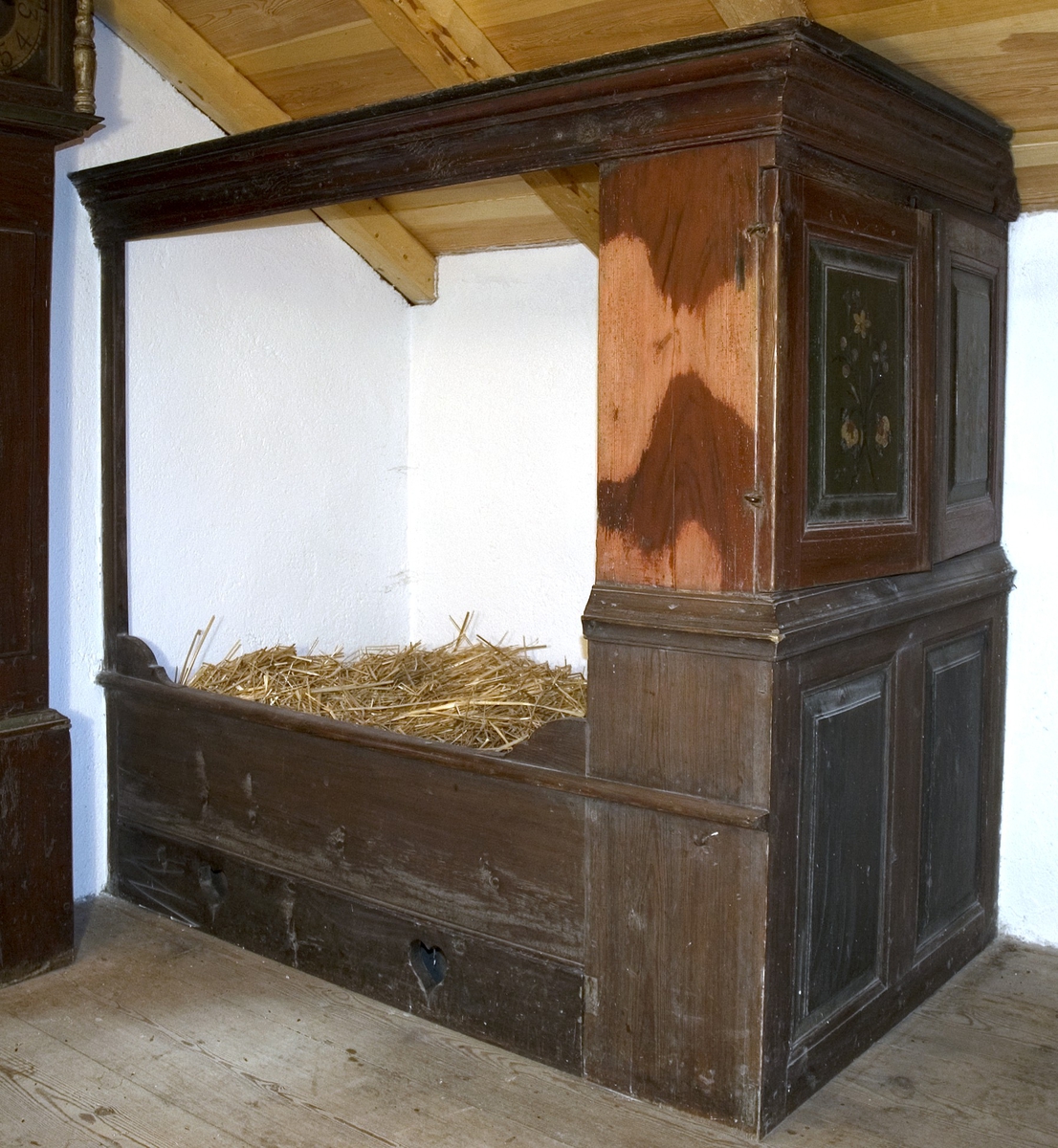 Skåpsäng, av trä. Profilerad ramlist upptill på fram- och sidostycke. Inget "innertak". Längs golvet en list med två utskurna hjärtan. Vid fotändens övre del finns ett skåp med två dörrar. Ett hyllplan i skåpet. Ovanför dörrarna finns en vridbar knopp för stängning. Nedanför dörrarna finns två fyllningar. Sängen är målad i brunrött med vissa detaljer och marmoreringar utförda i svart. Skåpdörrarnas fyllningar är målade med grönt som botten och därpå en enkel blombukett i vitt, rött och svart. Texten eller årtalet på höger dörr är bortnött, på vänster dörr står: L J D.