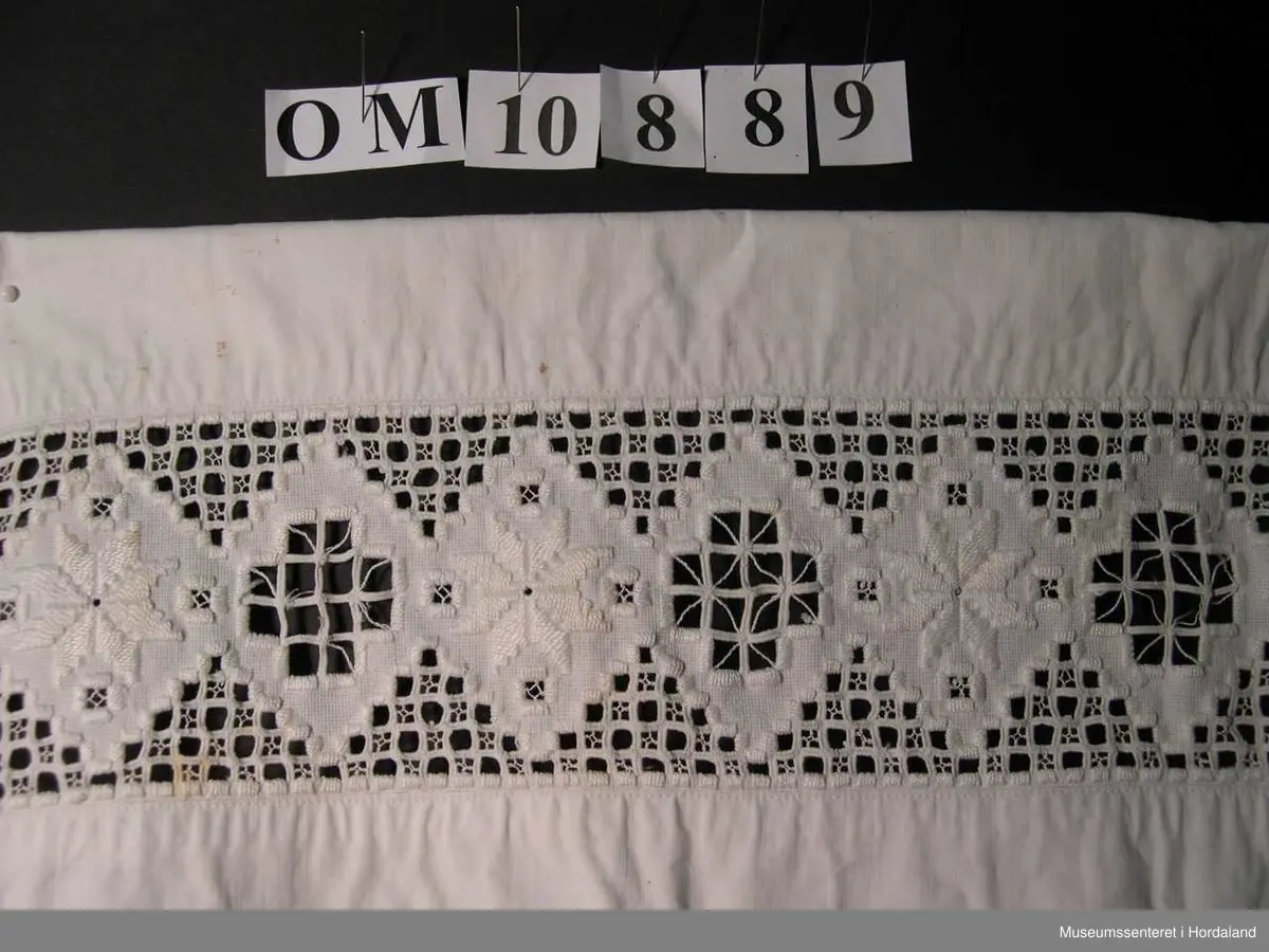 Form: bunadsforkle med linning og band i livet, knappa bak, innfeld broderi nedst på forkle
