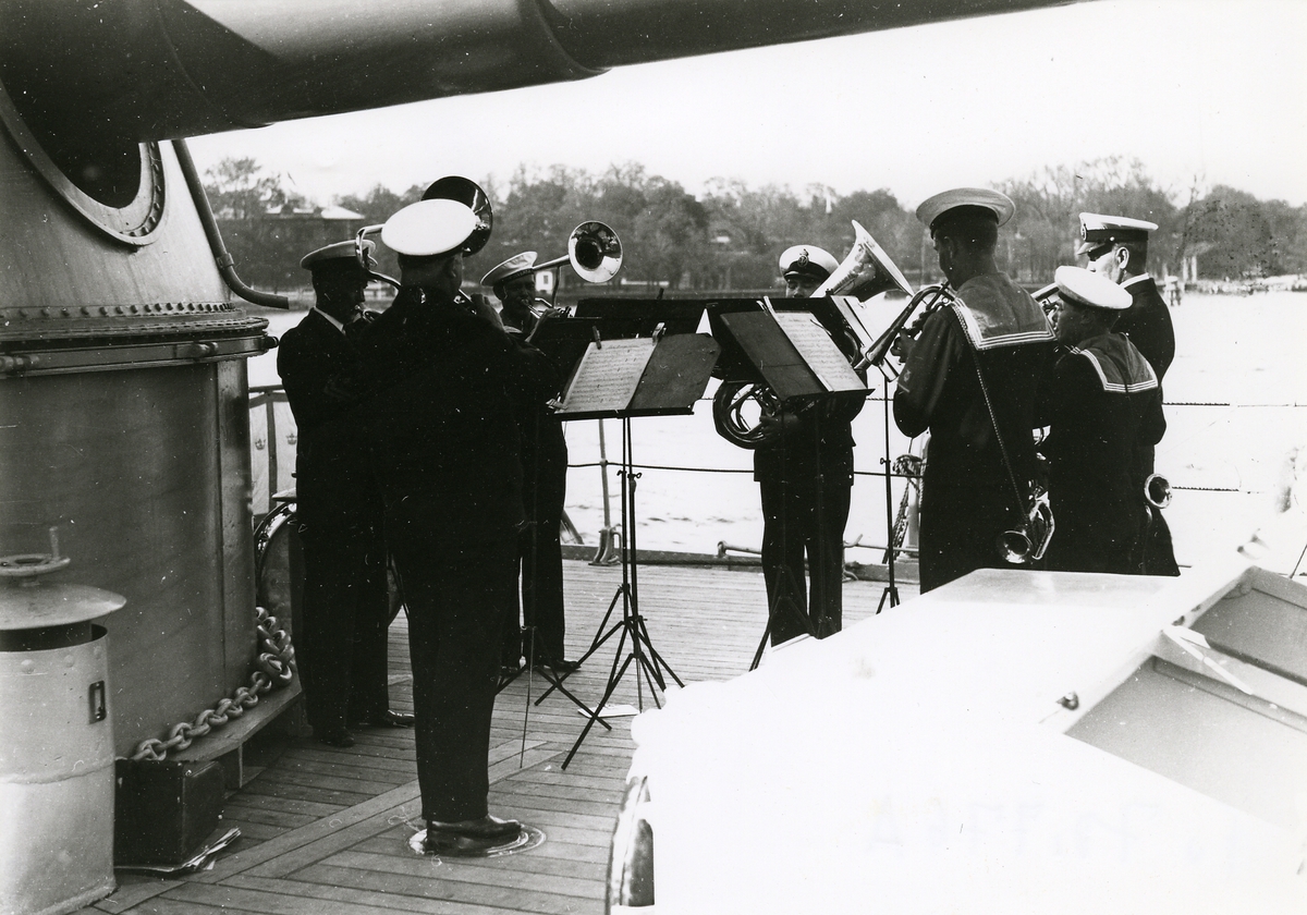 Blåsare musicerar ombord på örlogsfartyget Gustaf V. Pansarfartyget ligger förankrat på Stockholms ström.