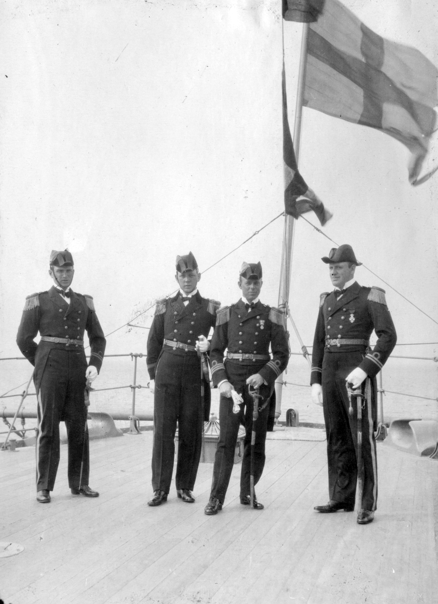 Sjöbefäl fotograferas på däck. I bakgrunden vajar svenska flaggan. Samtliga är klädda i paraduniform.