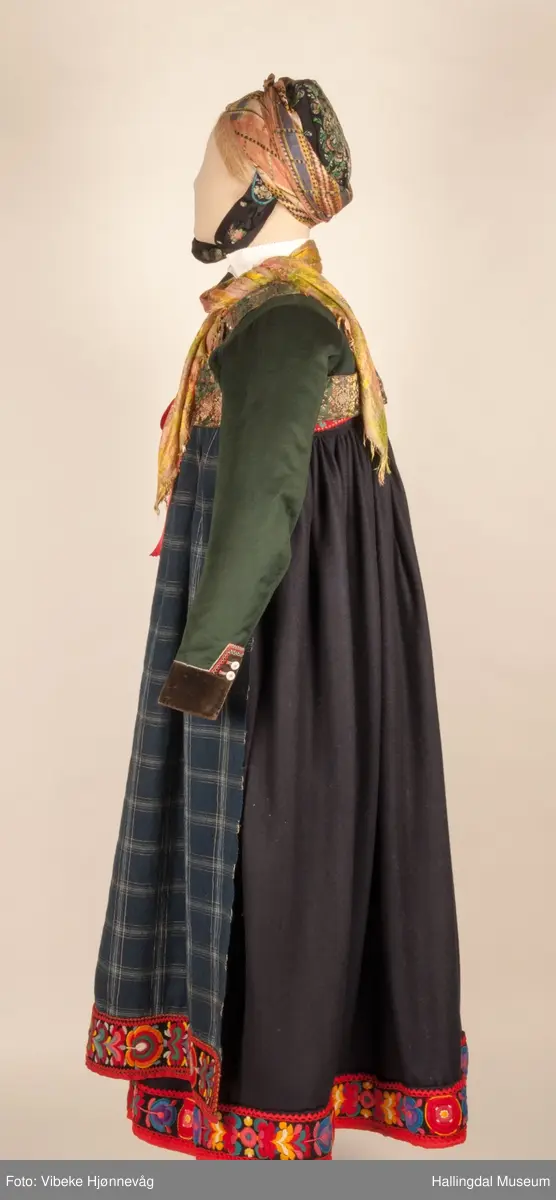 Kone fra Nedre Hallingdal i hallingbunad.  Kona står utstilt i den faste bunadutstillingen på Hallingdal Museum, Nesbyen.  Hallingbunaden består av mange draktdeler; trøya HFN 01835, Forkle HFN 03381, stakk, liv, lue, silketørkle rundt lua, silketørkle rundt halsen HFN 03500, bringduk og skjorte.