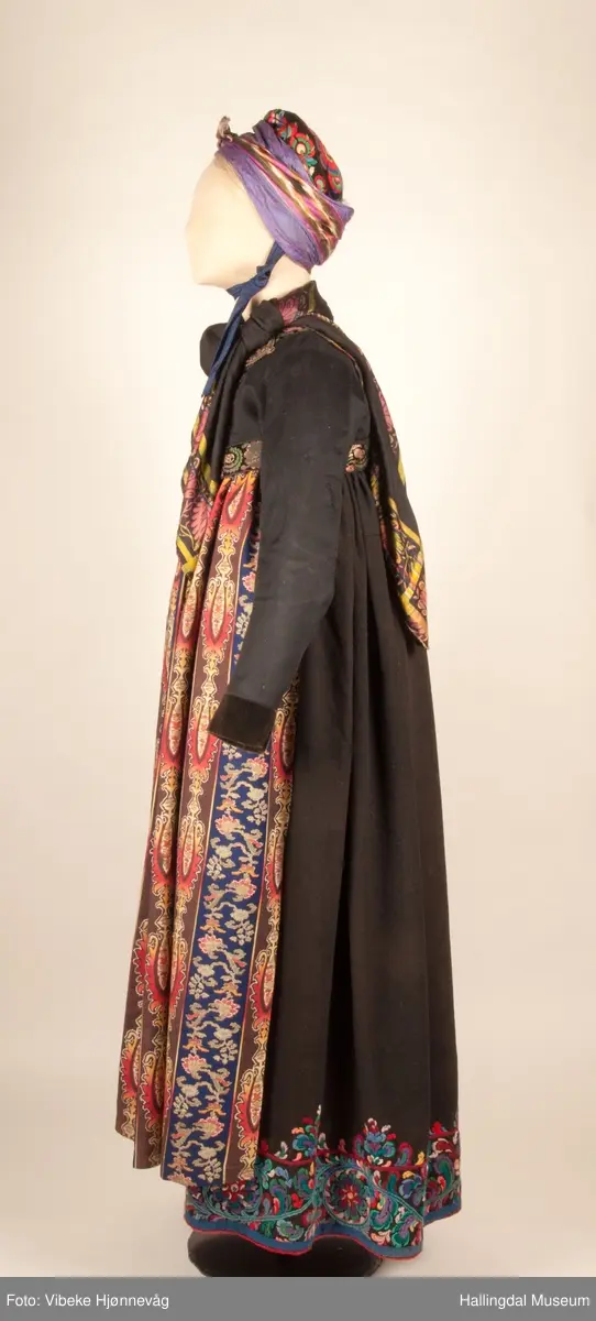 Kone fra Nedre Hallingdal i hallingbunad.  Kona står utstilt i den faste bunadutstillingen på Hallingdal Museum, Nesbyen.  Hallingbunaden består av mange draktdeler; trøye HFN 03608, Forkle HFN 02016, stakk, liv, lue, silketørkle rundt lua, silketørkle rundt halsen HFN 11158, bringduk og skjorte.