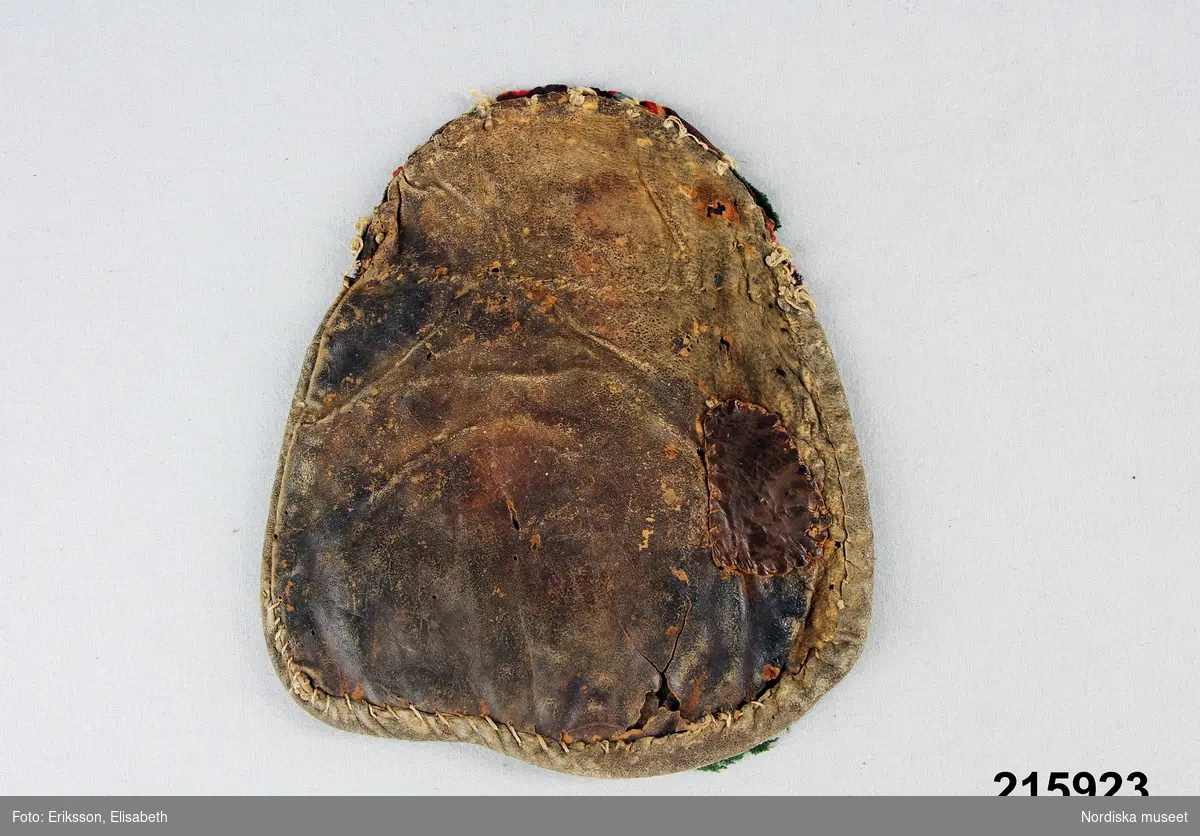 "Kjolsäck, framsida grön vadmal, röda applikationer, tennbroderier; baksida av skinn, bygel fattas."
/enligt intendent Inga Wintzells anteckningar