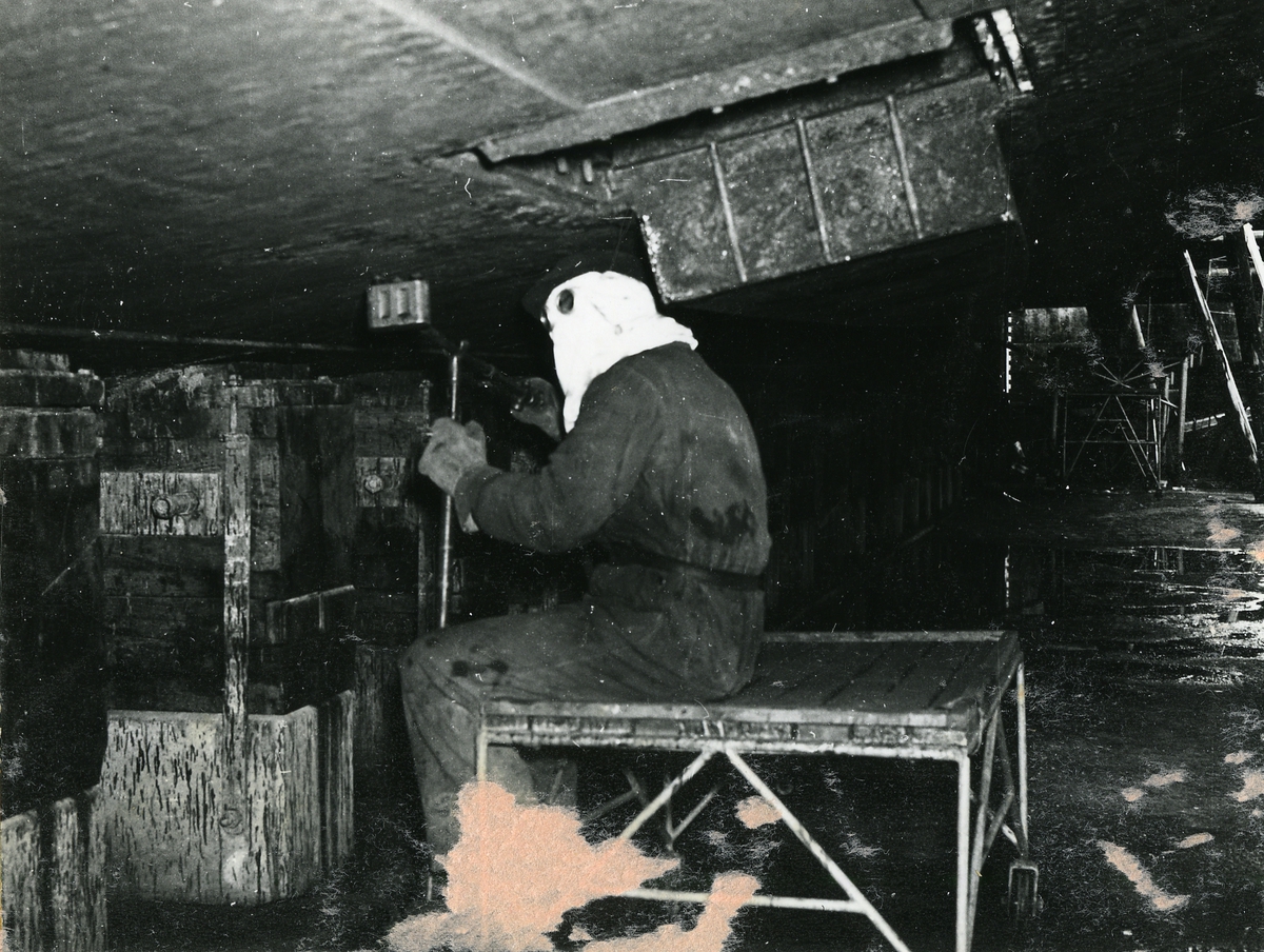HÄLSINGBORG
Jagare.
Rosthackningsarbete under fartygsbotten i torrdocka. Foto den 13 aug. 1957.