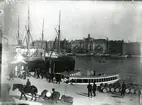 Foto från år 1900 eller något av det första åren av 1900-talet (1898) (Fotografi i Stockholms Stadsmuseum).
Vid Skeppsbron emellan Gustav III:s staty och Logårdstrappan ligga ångarna 