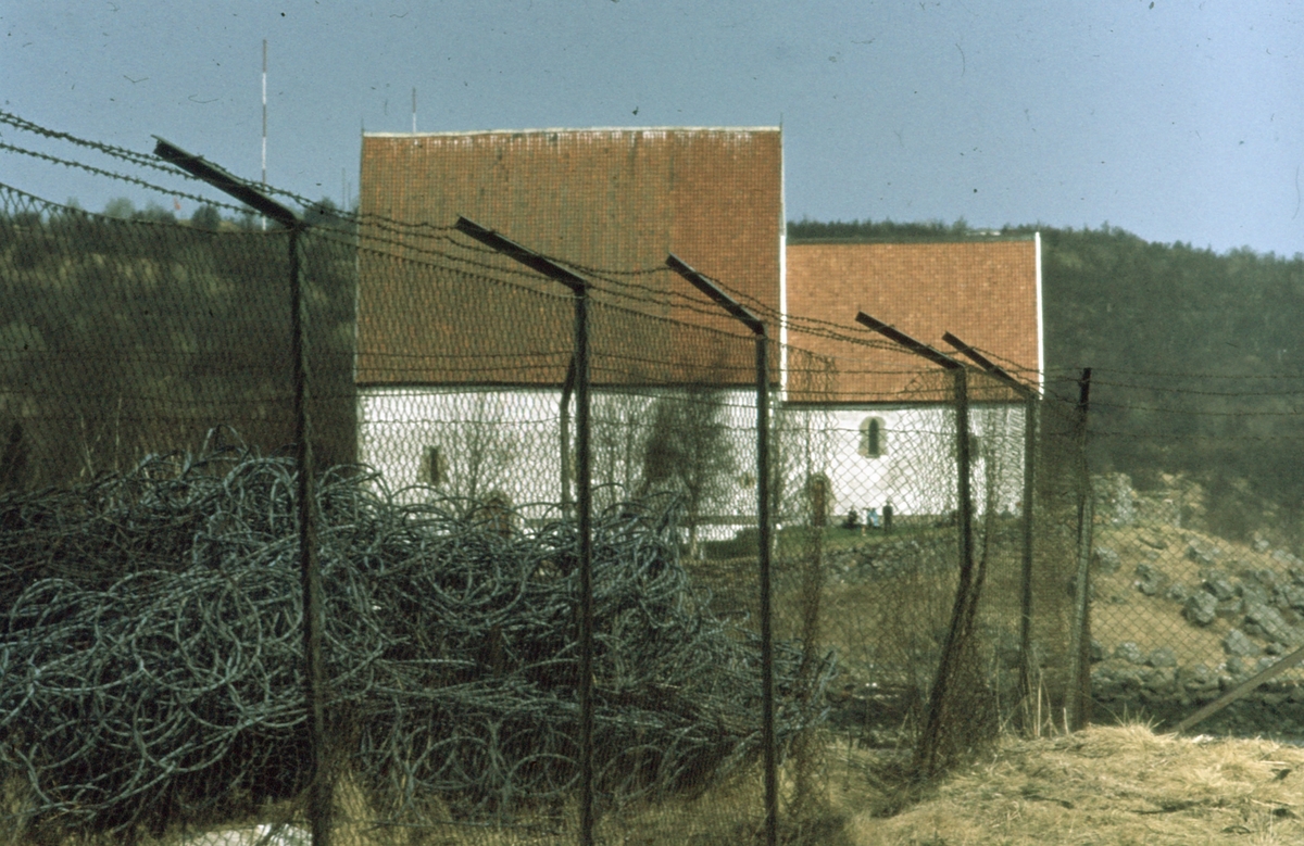 Trondenekirka fotografert fra "steinkaia", med høyt gjerde med piggtråd øverst i forgrunnen..