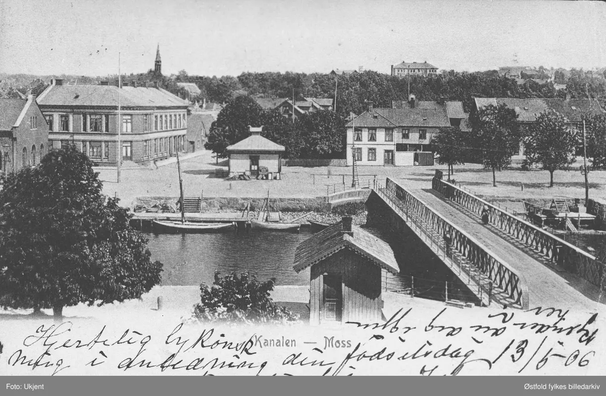 Kanalbrua i Moss, postkort fra før 1906.

Teglbygningen helt til venstre (nord) er tollboden. Den store murbygningen er Moss Kristelige Ungdomsforening, med adresse til Jeløgata.  I neste hus holdt urmaker Dahl til. Deretter fulgte meieriet (er ikke synlig på bildet. Bak Kanalkafeen til høyre kan vi se taket på Sykehusgaten 12, bolig i 2.etasjer med 4 leiligheter. I horisonten ses Moss kirke og Skarmyra skole.

Tollboden, (Jeløygata 2) bygget som synes helt til venstre i bildet ble bygget i 1858/59. Tollboden lå opprinnelig på Jernværket, før det flyttet til Storgaten(I dag Henr. Gerners gate). Der gikk lokalet med i den store bybrannen i 1958. På grunn av brannfaren ble nye bygg oppført i murstein. Blant annet Tollboden, som nå ble bygget ved kanalen. 

Neste bygg fra venstre, Jeløygata 4 har mye historikk. Det var Moss Ynglingeforening som i sin tid kjøpte eiendommen. De byttet senere navn til Moss Kristelige Ungdomsforening. 

Fiskebasaren, (Jeløygata 1) ble bygget i 1899. Her ble det solgt levende fisk. I 1961 flyttet de basaren på ruller, nærmere Tollboden for å gi plass til den nye broen som senere erstattet den på bildet. 

Kanalkafeen ble også revet for å plass til den senere Rådhusbroen. Kafeen var kjent for sitt lugubre selskap. Røyken lå ofte tykk med drankere og garva arbeidskarer side om side. (Arve Tomt Gundersen 2016")