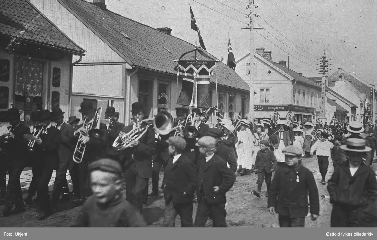 17. mai-tog antakelig,  i Nygaardsgata i Fredrikstad.  I forgrunnen ukjent musikkorps. Fane/flagg med påskrift ....bys Privatskole 1872, vanskelig å tyde. Det kan også være en pikeskole. Bygningen midt på bildet tilhørte Fredrikstad Blad.