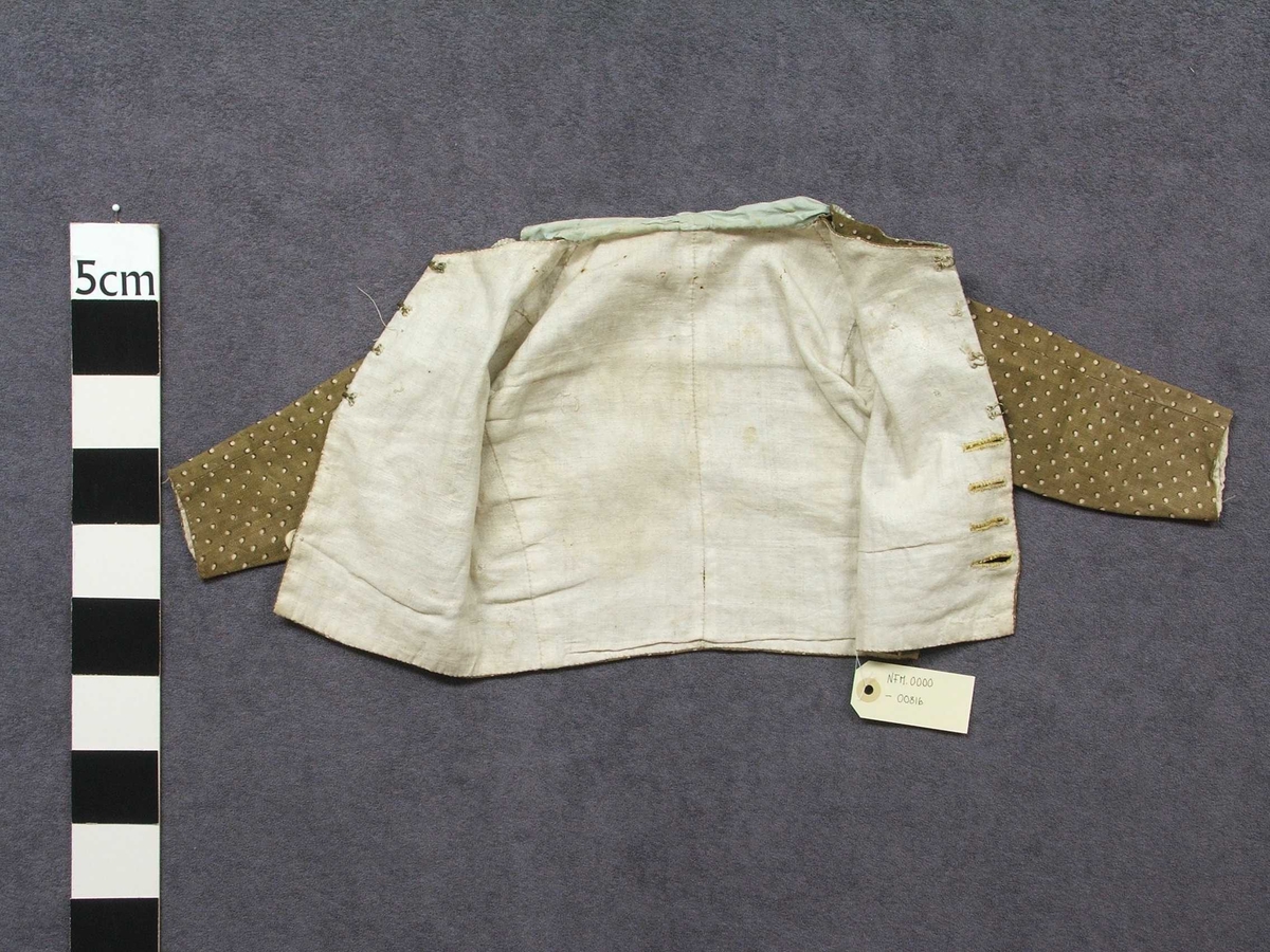 Jakke og bukse i bomullsstoff. Til gut. Høyrer saman som ei drakt.  Fôra med ufarga lin. Gul tråd i saum. Knappar i gull og svart. Buksa har klaff framme med tre knappar. Tre knappar nedst på kvart bein. Heilt nedst klaff med knapphol, her er knappane vekke. To knappar i lininga.  Knyting bak. Ein lapp i kvar side av lining. Jakka har silkeslag med påsydd pynt. Fire knapphol, berre ein knapp att. Fire hektar i heimelaga kvalitet til å hekta saman jakka øvst. På kvar side på jakka er det sydd på ein knapp med stoff.