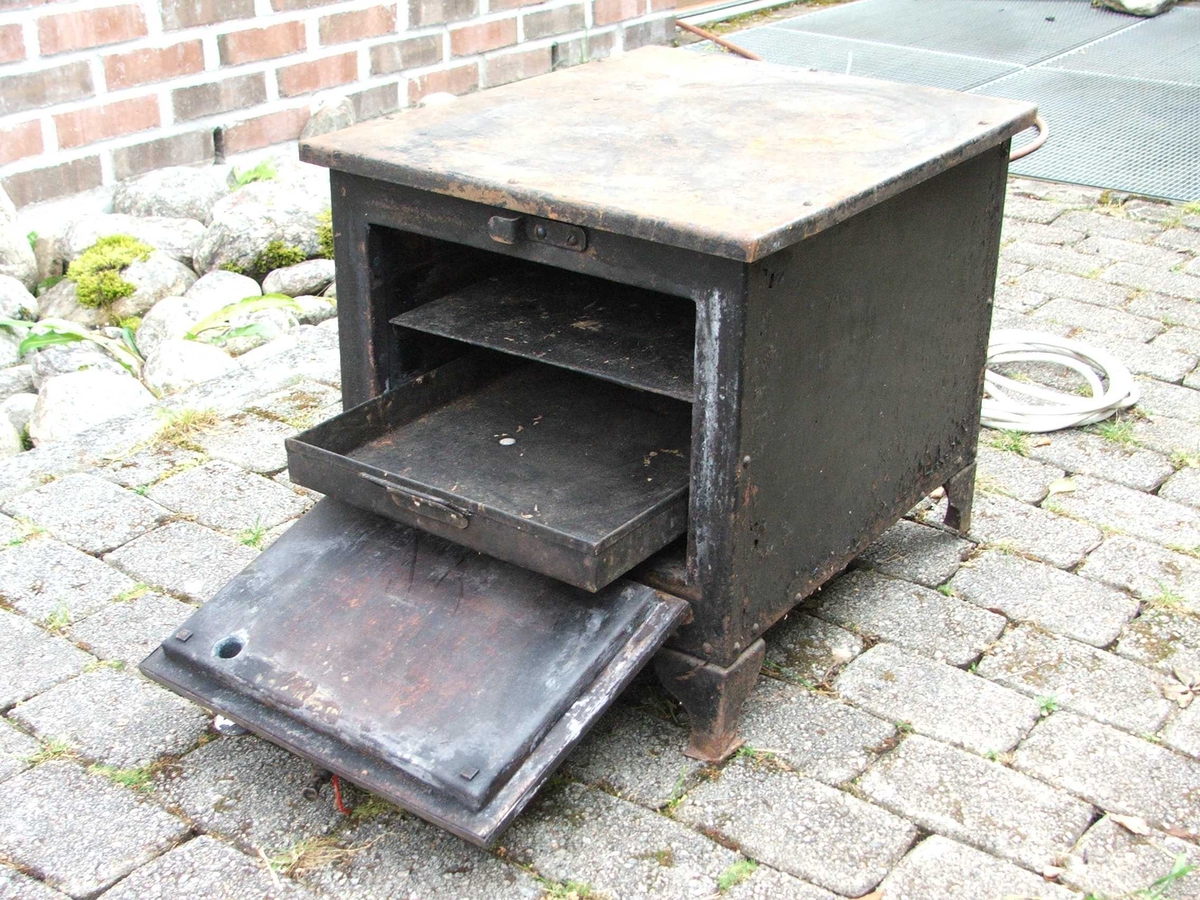 Elektrisk steikjeomn. Dør på eine kortsida med lukkemekanisme øvst. Tjukke veggar. Inni er det to lause steikjeplater. Det er spor til å setje plater på på veggane. Ei plate har kant, den andre ikkje. Øvst på eine langsida er det fire brytarar. Ledning kjem ut på kortsida bak.