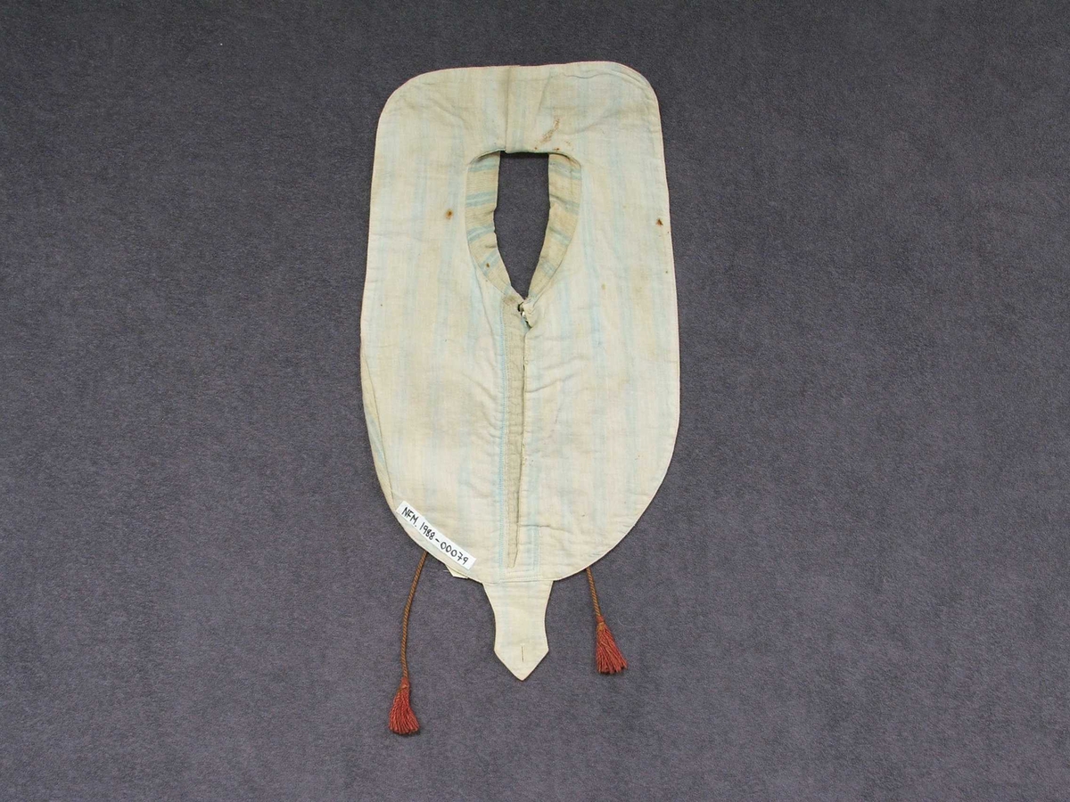 Skjortebryst. Oval form med knapping framme, opning til halsen, snippkrage med knappar ned på stoffet under. Nedst midt framme er sydd på ei "tunge" med knapphol i same stoff. Stoffet har lyseblå og kvite striper. Fôra med einsfarga stoff. Pynteband på krage og knappestolper med grønt og rosa. Brunraud snor m/duskar rundt halsen og heng ned framme.