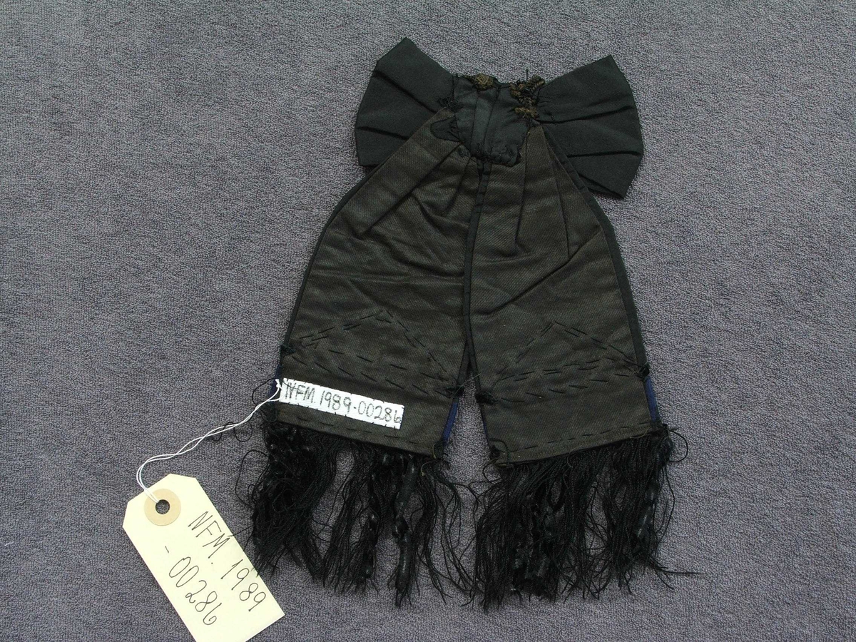 Svart sløyfe, pynt til bluse eller hovudplagg. Silkefrynser, fløyelsband, glasperler sydd på. Fôra.