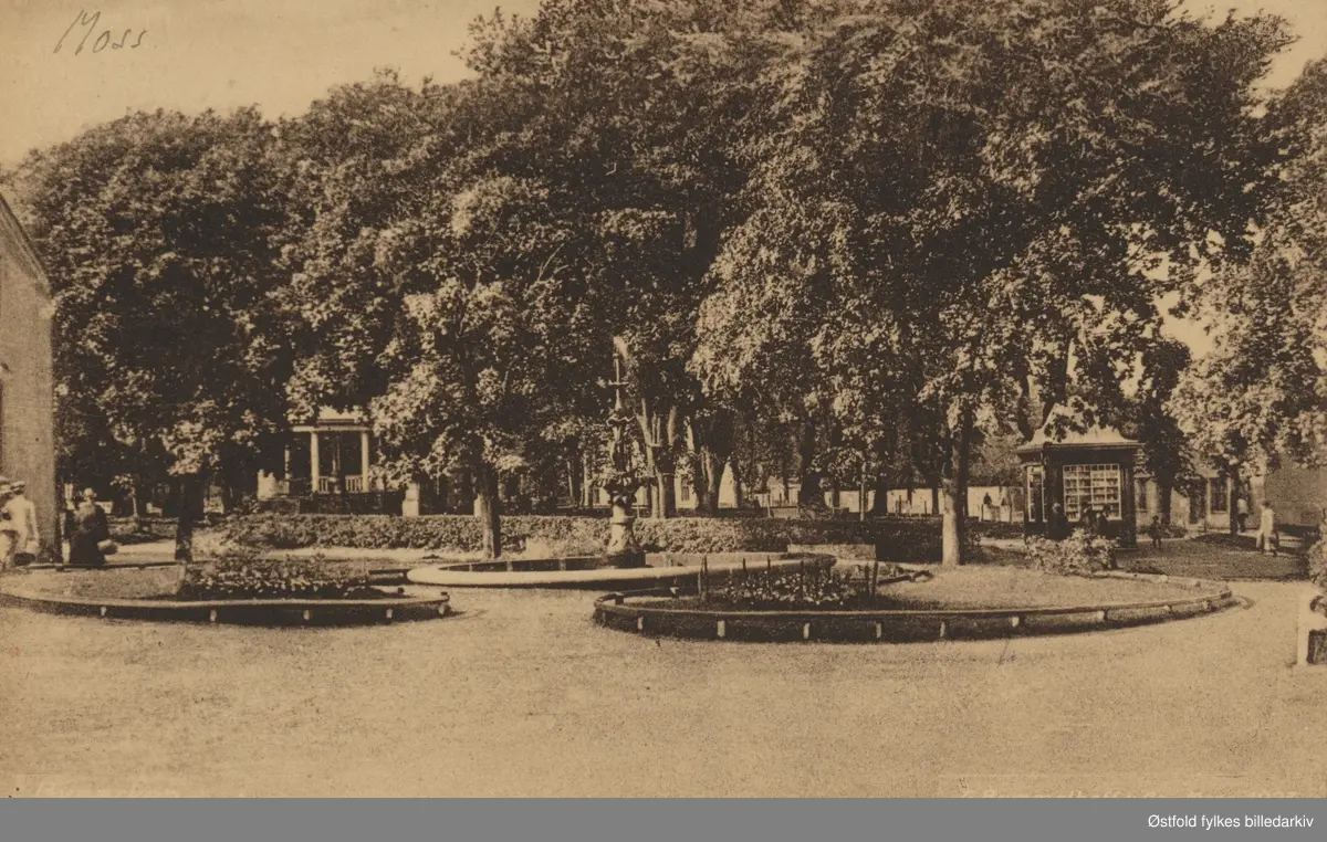Kirkeparken  i Moss med den gamle fontenen som ble fjernet i 1936. Paviljongen og en kiosk. Tittel på postkortet: "Byparken."