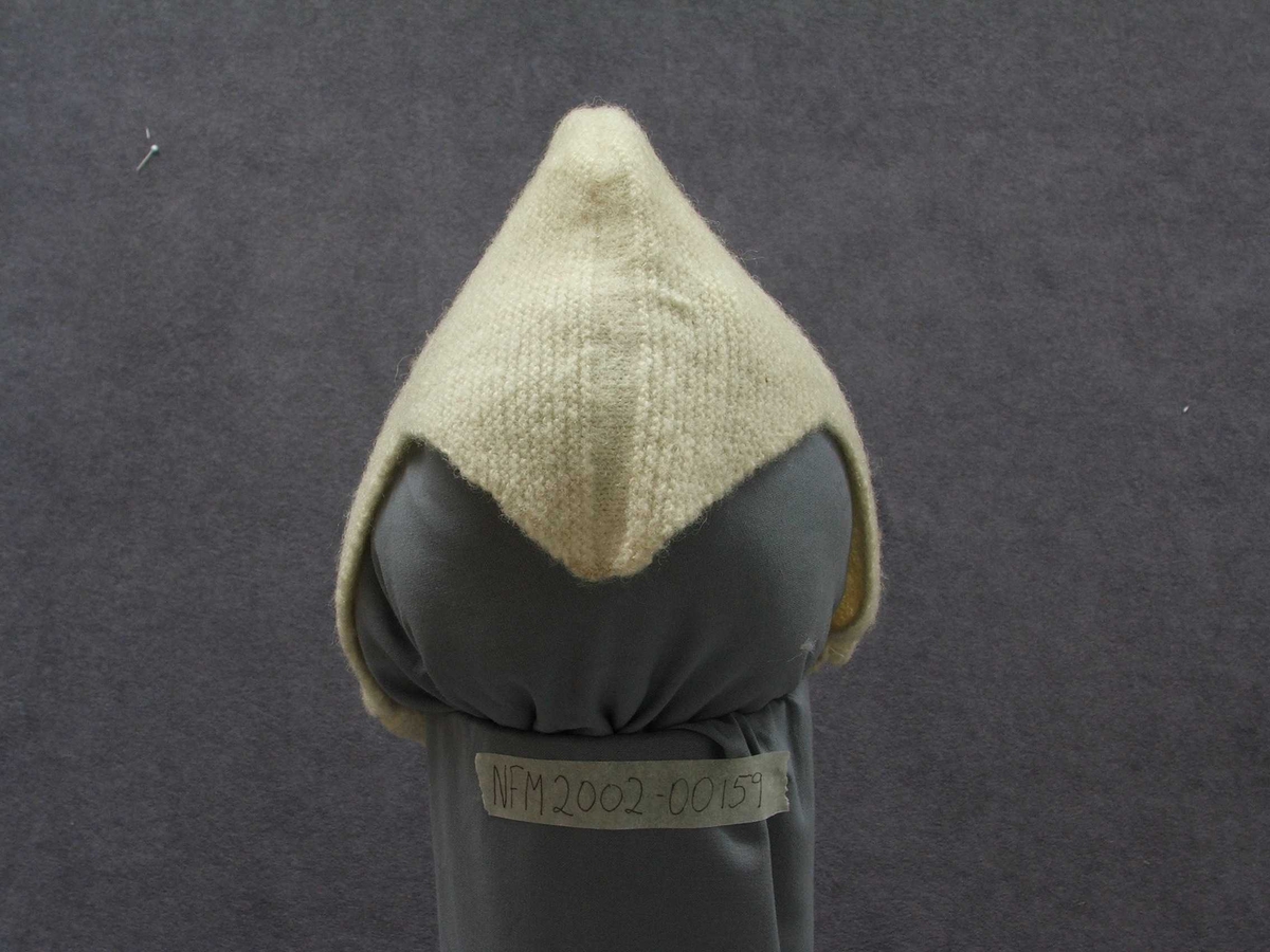 Strikka barnehue. Slags hjelm-fasong med ein spiss ned i panna. Strikka band til å ha under haka og knappe fast på andre sida.