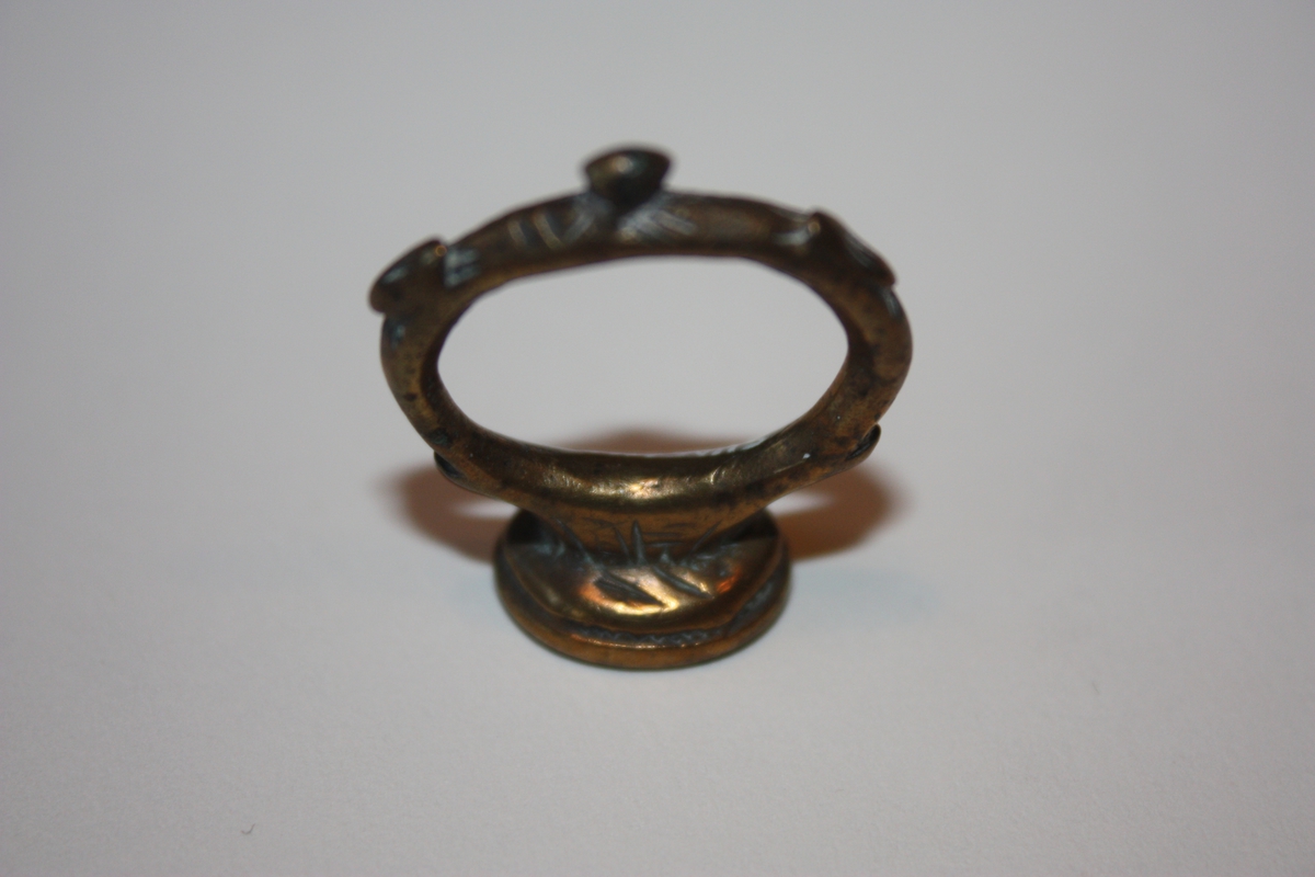 Ring med oval signetplate. Inngravert APS med bumerke under. Enkel strekdekor på oversida av plata. Små utposingar på ringen