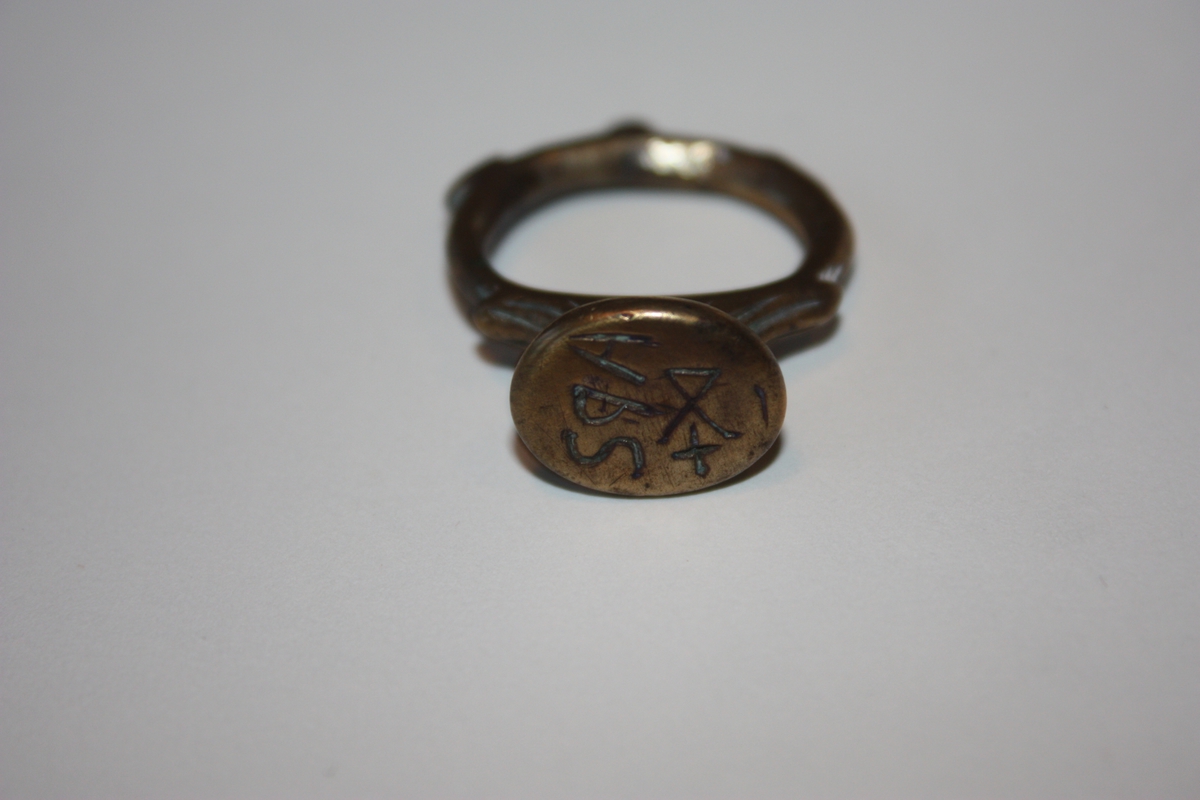 Ring med oval signetplate. Inngravert APS med bumerke under. Enkel strekdekor på oversida av plata. Små utposingar på ringen