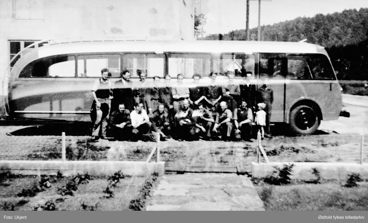 Avhenting av ny buss i Mandal til Mørks Bilruter, Skiptvet,  ca. 1955.
Abram Sangvik, fabrikkeieren, står som nr. 2 fra venstre i bakre rekke. Dette ifølge sønnen hans, Odd Sangvik. 

Mandal skulle tilsi at bussen er bygd ved A. Sangviks karosserifabrikk der. Kfr. Asbjørn Rolseth: Håndverk på hjul s. 570 ff. Linjeføring på frontpartiet tilsier trolig at foto er litt eldre, ca. 1950. (Ivar Stav 2016)