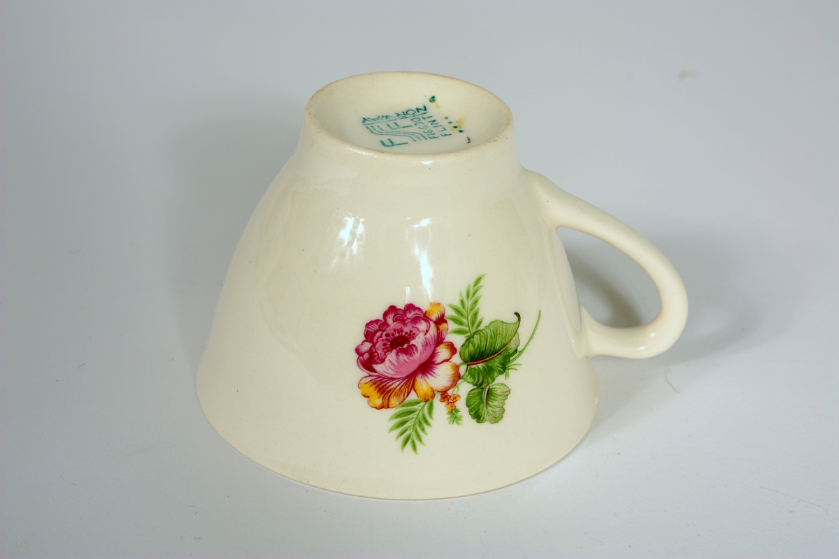 Fiolett blomster m/grøne blad, ein stor på venstre og ein mindre på høgre sida av hanken.