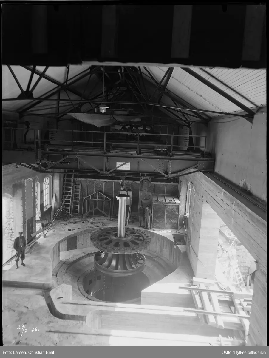 Ukjent interiør, 29. juli 1936.
Typisk kraftstasjonsinteriør med traverskran som spenner over hele rommet, her i ferd med å løfte/senke vertikalmontert turbin. Kan det være fra ombygging av Hafslund kraftstasjon? Til venstre rekke med typiske industrivinduer fra før/rundt 1900.