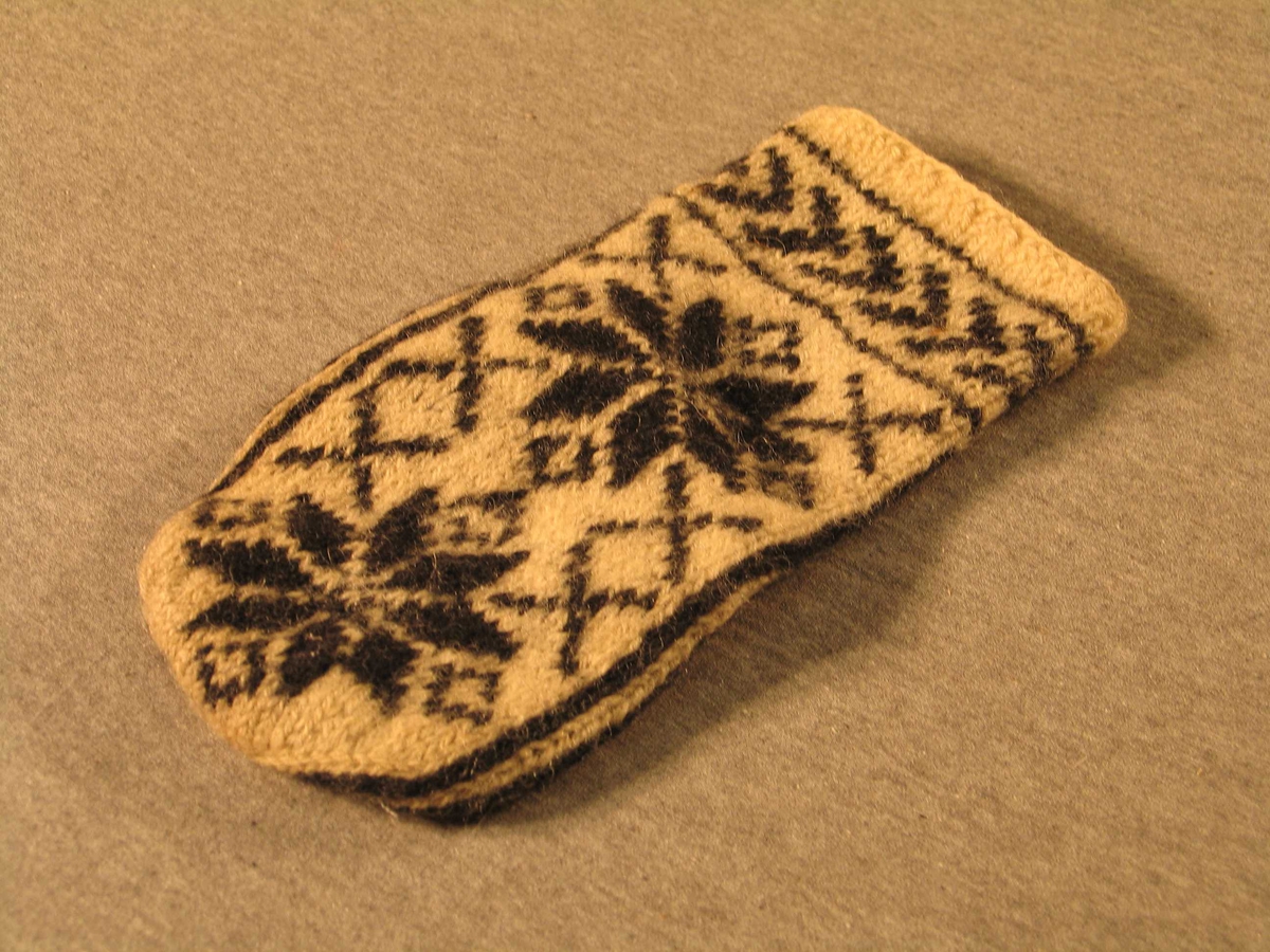 Handstrikka venstre-vott i såkalla selbumønster. Brot med to rette og ein rang over 2 omgangar, eit felt med liggande v-ar og sjølve votten med to store åttebladroser.