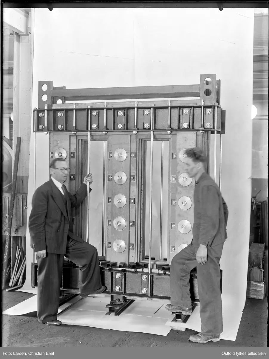 Produktfoto av transformator, 1945, Kan ha tilknytning til Rich. Pfeiffer, elektrisk verksted og transformatorfabrikk, Vestengveien 40 i Sarpsborg. Eneste i sitt slag i byen, kfr. s. 578 i Sætherskar: Det norske næringsliv. Østfold fylkesbind, Bergen 1951. Mannen til venstre er kanskje eieren, Rich. Pfeiffer (død 1946) eller hans etterfølger, ingeniør Erik Hox.

Arne Andersen 2013: Kan dette bildet ha sammenheng med objektet
ØFB.CLA.UNR.00917 ?
