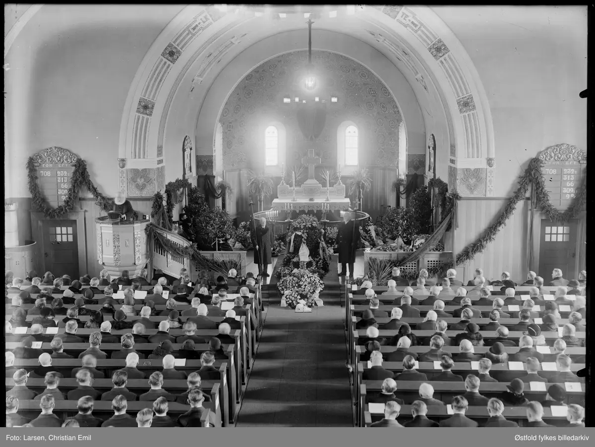 Begravelse i Tune kirke, Sarpsborg i mars 1932. Begravelsen til statsminister Peder Kolstad som døde 5. mars. Krans fra Kongen og Dronninga. Pynta med girlander av granbar og sørgeslø i sort, to marskalker stilt opp foran kista. 
Krans fra Landmannsforeninga i Sarpsborg.  

Peder Ludvik Kolstad, født i Borge, politiker for Bondepartiet, statsminister  fra 12. mai 1931 til 5. mars 1932. Fra 1912 var han bestyrer ved Kalnes landbruksskole. 1922-32 stortingsrepresentant fra Østfold fylke; odelstingspresident 1931 og samme år statsminister og finansminister i Bondepartiets regjering. Kolstad ble imidlertid syk og døde etter et knapt år som statsminister.