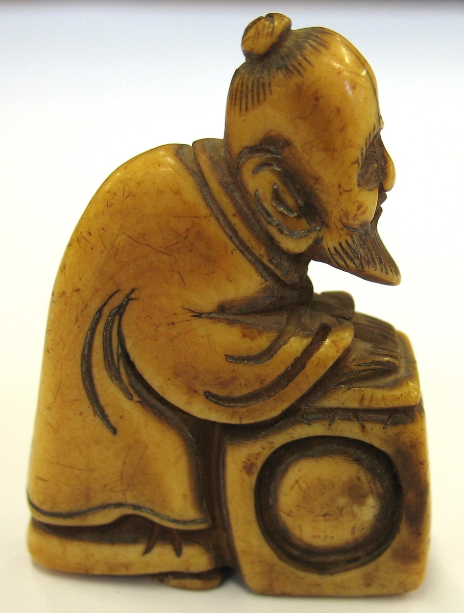 15 368:081: Netsuke ( man med spetsigt skägg och låda).
En netuske är en form av miniatyrskulpterad knapp i olika material.  Eftersom den traditionella japanska dräkten saknade fickor så fick denna knapp både en praktisk och prydande funktion som mothåll till hängande föremål som bars vid bältet.