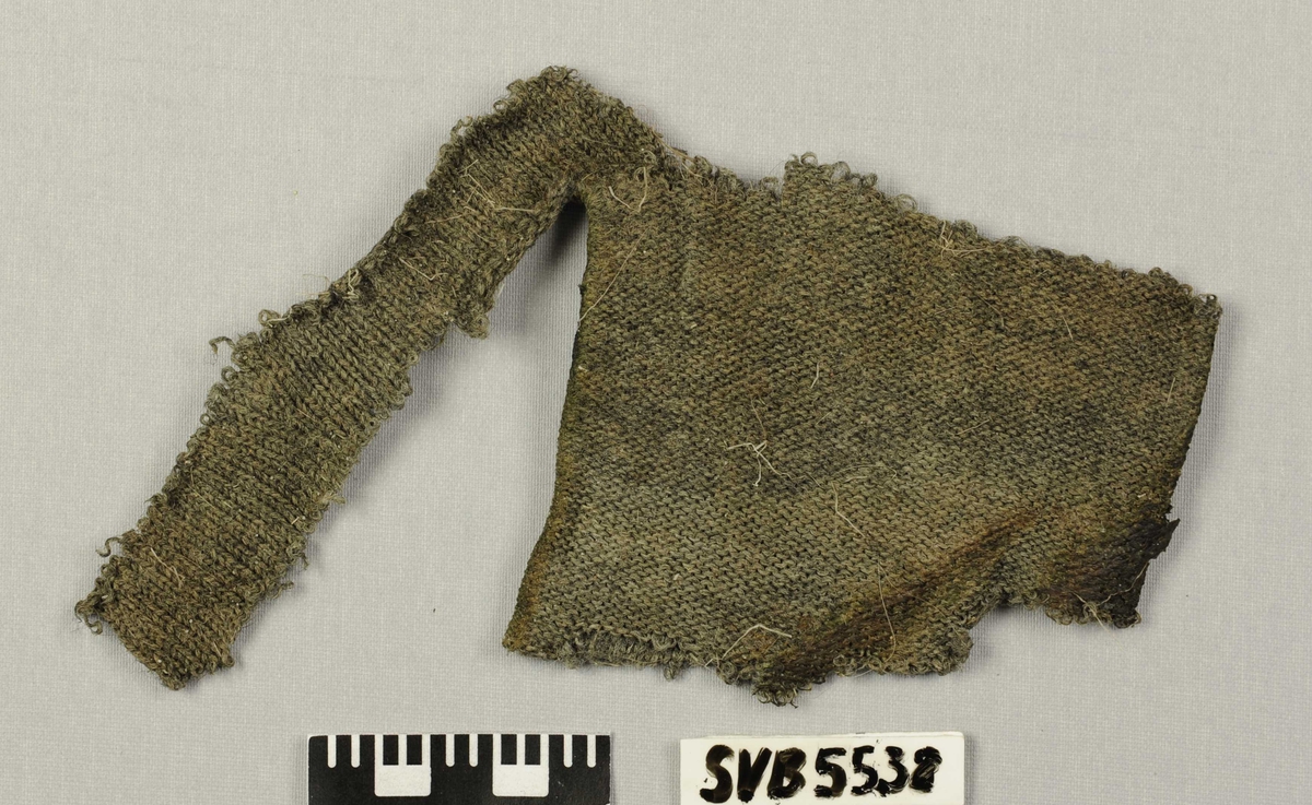 Strikket tøyfragment som kan være del av et bekledningsstykke. Det er strikket rundt og kan være del av et erme eller sokk. Det ser ut som maskinstrikket. Fragmentet er slitt.
