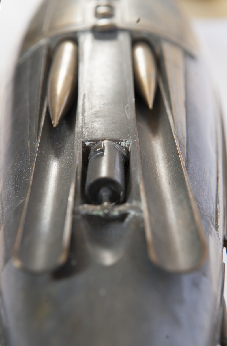 Spolformad. Stålplåt. Slingerköl, 2 propellrar av metall, 2 st höjd- och sidoroder parallellkopplade med gardjärn. 2 st höj- och sänkbara periskop av mässing. 4 st rännor för torpeder, därav 2 med luckor framtill, dels 2 för magasinering. Kort cylinder, rörlig i ränna midskepps akterut. Torpedrännorna täckas av långa stållock. Tillhörande 4 st torpeder av massiv mässing. Eneroths förslag till ubåt 1897. UndervattenstorpedFöremålets form: Spolformad.