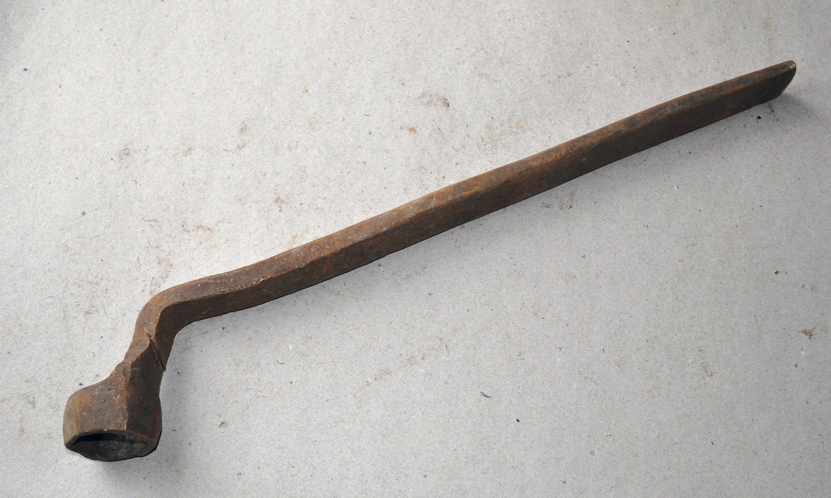 Håndsmidd sekskant fastnøkkel av jern, med 1 1/2" lukket kjeft. Langt håndtak av jern, med en bøy på halsen. Fastnøkkelen er smidd av et flattjern.