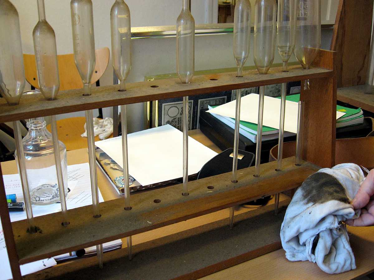 9 glassrør, med kul (kolbe) på midten og pipette-hull i den ene enden. Det er plass til 2 rør til i trestativet.