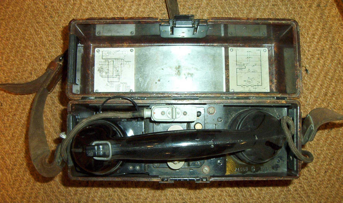 Felttelefon. Feldfernsprecher 33, FF33, tyskprodusert. Serienummer 74058.  Produksjonsår 1941. Telefonen er innebygd i bakelittkasse med bæresele. Hvit kodelapp montert på lokket. Det tyske alfabet står skrevet på lokket.
