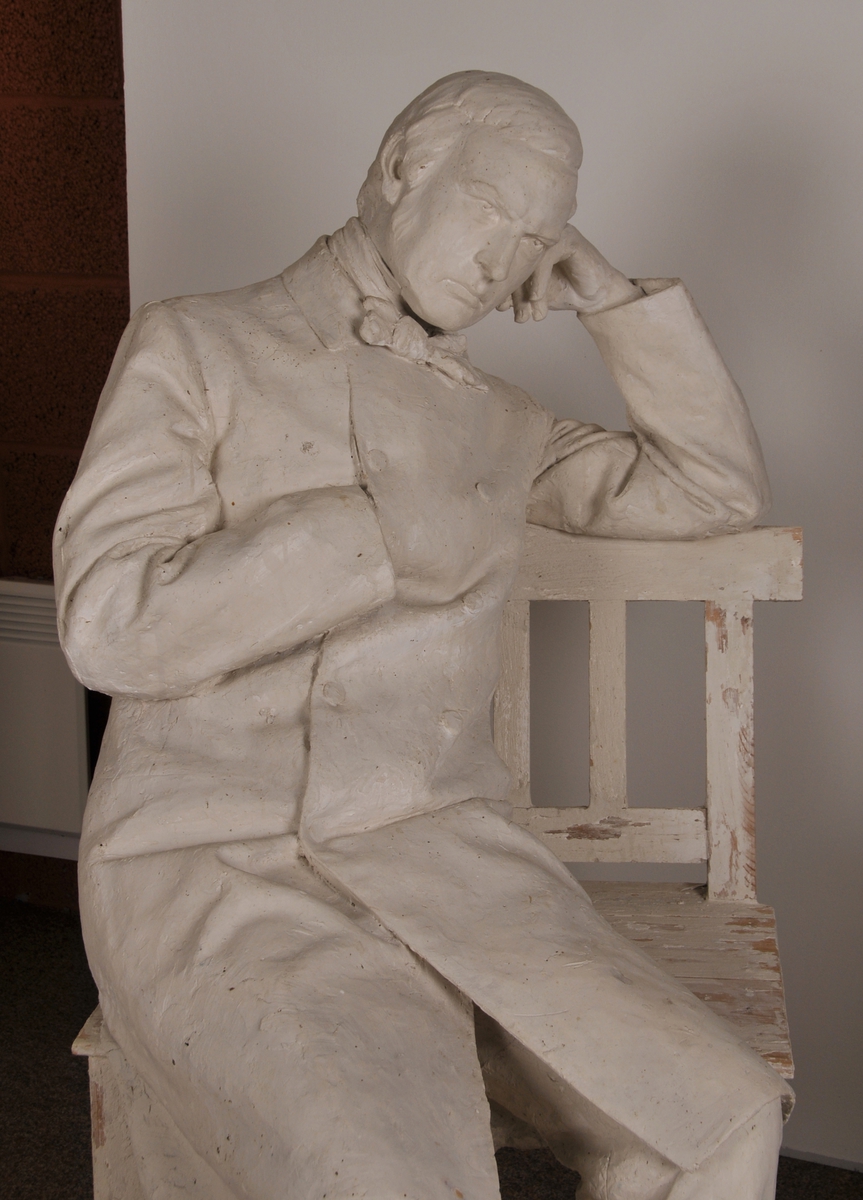 Heilfigur av diktaren J. S. Welhaven, sitjande på ein benk. Motto frå verset "det er en bitter kvide".