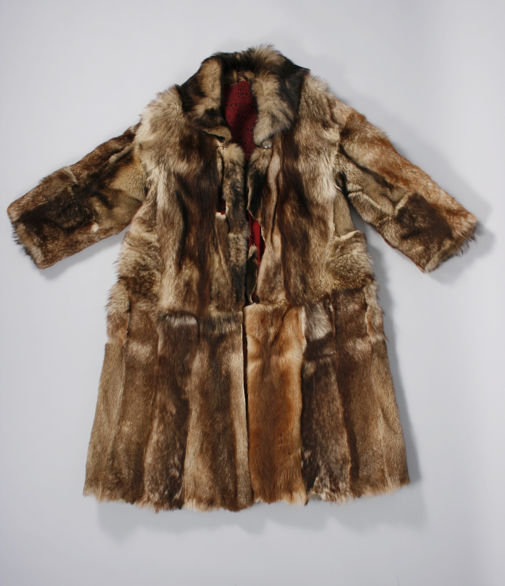 Ulveskinnspels, Lang og noe utskrådd. 
Sydd sammen av mange smale pelsstykker, to i høyden. En liten splitt midt bak. Ermer sydd sammen av mindre pelsstykker. Ermene har en liten oppbrettet fald av pelsen i nedkant, på resten av plagget er pels og fór sydd sammen kant i kant, ute belegg eller oppbrettet fald. Sjalskrage med underkrage av sort kunstpels. Underkragen har søm midt bak. 
Fóret med rødt klede med sort trykk, også i ermene.
Hele plagget er håndsydd med grov tråd, selve pelsen med ubleket lintråd. Fóret er sydd sammen, og sydd til pelsen, med ubleket eller sort bomullstråd. Fóret har sidesømmer, men ingen søm i ryggen. Ryggstykket er kvadratisk med trådrette sider. Forstykkene er trådrette midt foran og skrådd i siden. I sidene er det satt inn en liten kile nederst. 
I nedkant av kragen i venstre side er det en stor sølvhekte, gravert med blomstermotiv. Ingen tegn til annen lukning.  
Stor lærhempe i nakken.