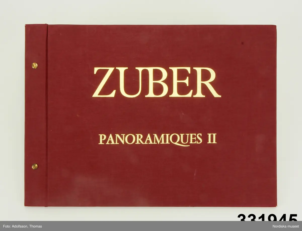 Tapetprovbok med vinröd pärm. På pärmens utsida, text i guld: "ZUBER PANORAMIQUES II". På försättsbladet: "ZUBER & CIE Impression à la main de papiers et tissus de Haute Décoration. Rixheim-Alsace- France. Depuis 1797".

Provboken innehåller prover på panoramatapeterna Pompei, Atrium, De 4 årstiderna, Golfo di Napoli, Les Antilles, La Grece, La Chasse och Terasses Romaines. Motiv ur tapeterna presenteras i sin helhet genom fotografier där vådernas mått och motivets hela mått redovisas. Ett par prov av produkten, två färgalternativ av ett stycke tapet som föreställer ett fartyg, på tapeten Les Antilles.

Panoramatapeterna består av motiv i 2-7 våder i bredderna 140-490 cm. Totalhöjd 290 cm. Priset på tapeterna var 1988 4787-17190 kr/ motiv.

På insidan av pärmen en prislista.
/Maria Maxén 2013-10-08