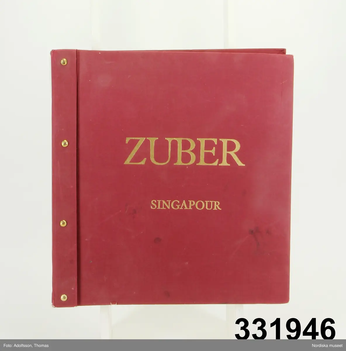 Tapetprovbok med vinröd pärm. På pärmens utsida, text i guld: "ZUBER SINGAPOUR". På försättsbladet: "ZUBER & CIE Impression à la main de papiers et tissus de Haute Décoration. Rixheim-Alsace- France. Depuis 1797".

Provboken innehåller prover på handtryckta papperstapeter och samkomponerade tapetbårder i klara starka färger, ofta mot vita eller ljusa bottnar. Det flesta tapeterna har täta vegetativa mönster med blommor, blad och fåglar. Spaljémönster, kakelimitationer samt figurativa mönster med asiatiska män och jaktmotiv med turbanklädda jägare med sablar och pilbågar. 

På  pärmens insida prislista över tapeterna i "Kollektion Singapour" från 1999. Där framgår att tapetmönstren heter Bambou, Pergola, Bahamas, Djakarta, Les Dauphins, Les Oiselets, Trellis Fleuri, Feuillantine, Pigue Nique, Chekou, Chinese, Perse, Chasse Persanne och Kabuki. Bårder: Frise pomme de pin, Bordure Bambou, Frise Torsadee, Bordure Grecque, Bordure Buis, Bordure Perle, Bordure Lierre, Bordure Roses och Bordure Epi de Ble.
Priset på tapeterna var 1999 736-464 kr/rulle exklusive moms. Bårdernas pris: 40-185kr/m.

Anm.
Pärmens framsida något fläckig.
/Maria Maxén 2013-09-25