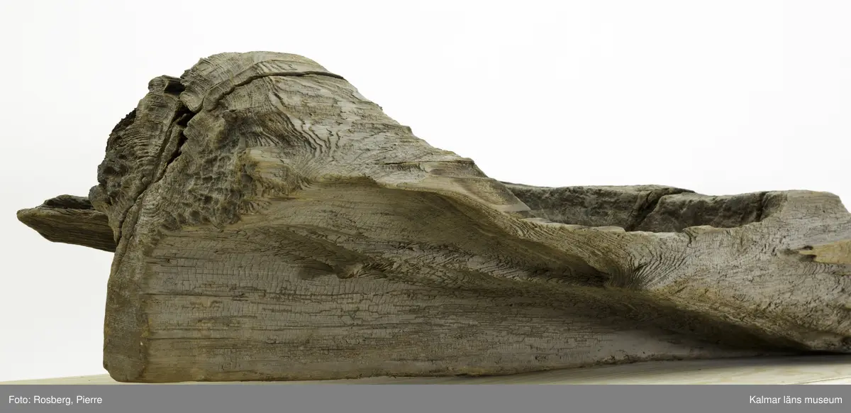 KLM 9303. Båt, stockbåt. Av urholkad trädstam. Huggen i ett stycke. Den har subrektangulärt tvärsnitt, dvs. rektangulär form med rundade kanter. Båten är formad med ett mittre djupare rum med högre för- och akterpartier. Mittpartiet är avgränsat med vertikala tvärväggar, skottar, som utgörs av den bibehållna stocken. Den bakre tvärväggen är högre och har troligen använts som toft. I aktern en köl som sträcker sig fram till ungefär mitten av båten. Framför tväravsatsen i aktern, toften, finns babord om kölen ett rektangulärt hål 15 x 6 cm i botten. På båten en beläggning, troligen sediment från sjön den hittades i.