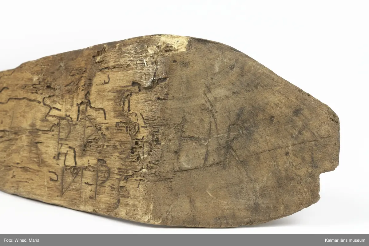 KLM 15141. Skära, vinkelskära, trä, metall. Vinkelskära med bågböjt blad av järn, fastnitat på skaftets ena sida. Skaft av trä med handbygel. Bladet är målat i rödbrun färg, för rostskydd, under senare tid. Inristning skaft: KPA, NPS HR. Stämpel blad: lis ?