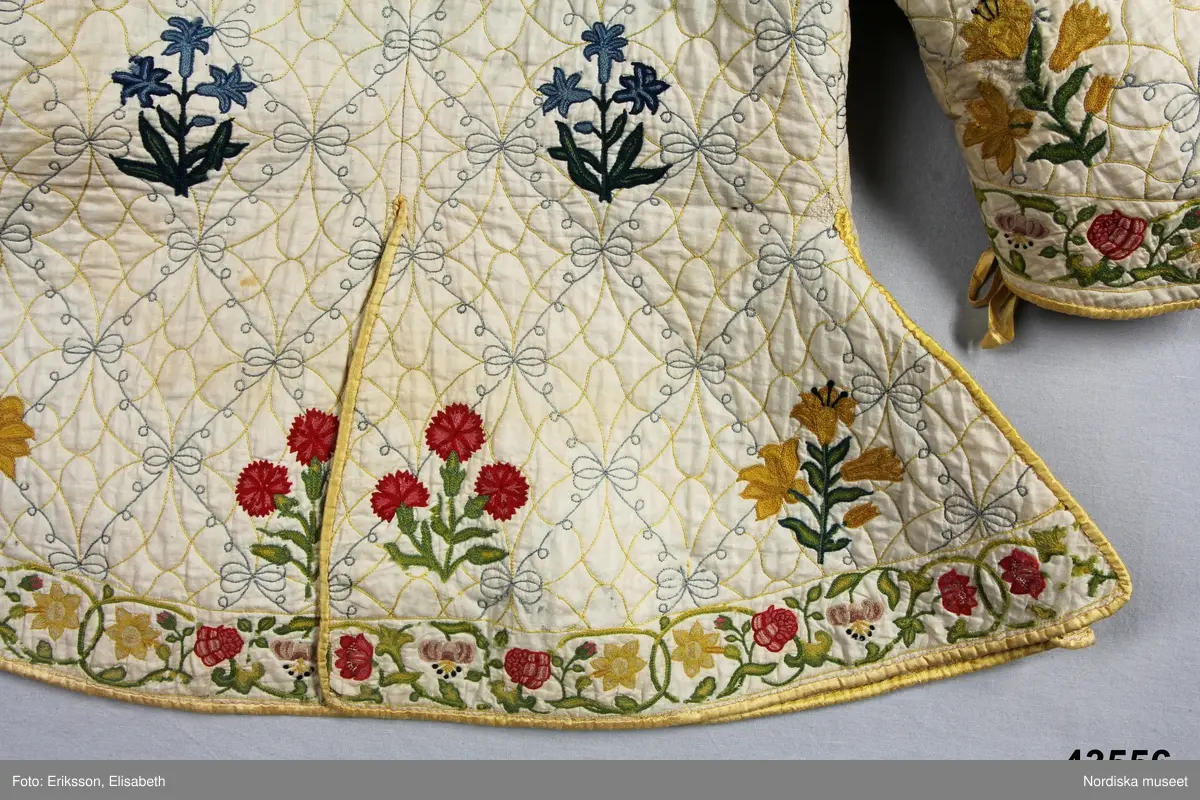 Katalogkort IV:
"Tröja / kofta, för dam, 1600-talets slut.
Längd 54 cm
Av linnelärt med foder av glest tuskaftat ylletyg. Försedd med stickningar i gult och blått samt broderier i kedje-söm med yllegarn. 2 ryggstycken, 2 framstycken. Halvlånga ärmar med 2 sömmar, varav den ena öppen och kantad med gult siden samt försedd med gult silke tränsade snörhål, med band av dubbelvikt sammansytt band. Sömarna uppslitsade nedifrån upptill midjan och kantade med gult siden."