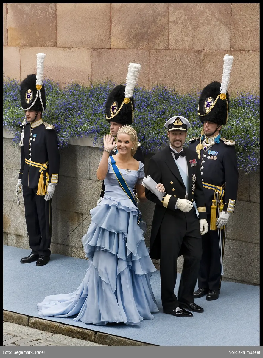 Kronprinsessbröllopet. Dokumentation av bröllopet mellan Kronprinsessan Victoria och herr Daniel Westling 19 juni 2010. Gästerna anländer till Storkyrkan. Kronprins Haakon i stor mässdräkt och ordenstecken med makan kronprinsessan Mette Marit i blekblå chiffonklänning med volanger, diadem, smycken, grå kuvertväska, och ordenstecken.