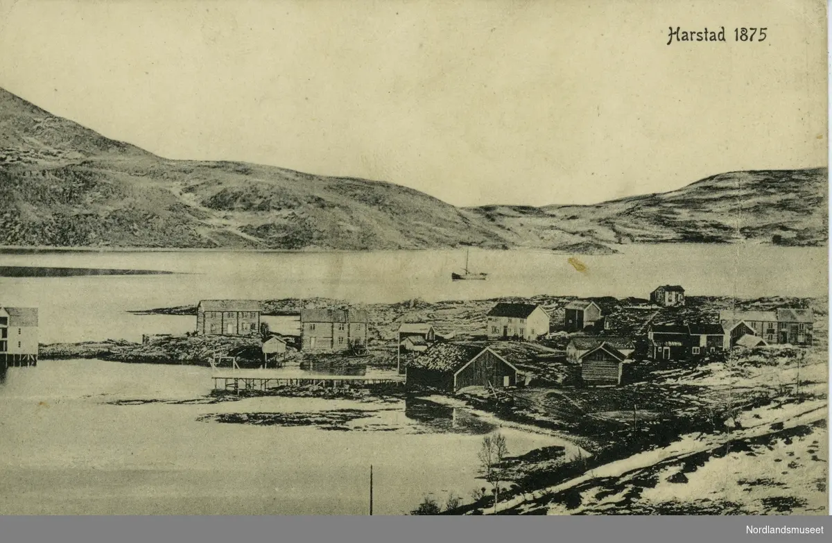Postkort som viser Harstad anno 1875. Bygninger ligger ved sjøen, fjell i bakgrunnen. 

Bakside: Blank.