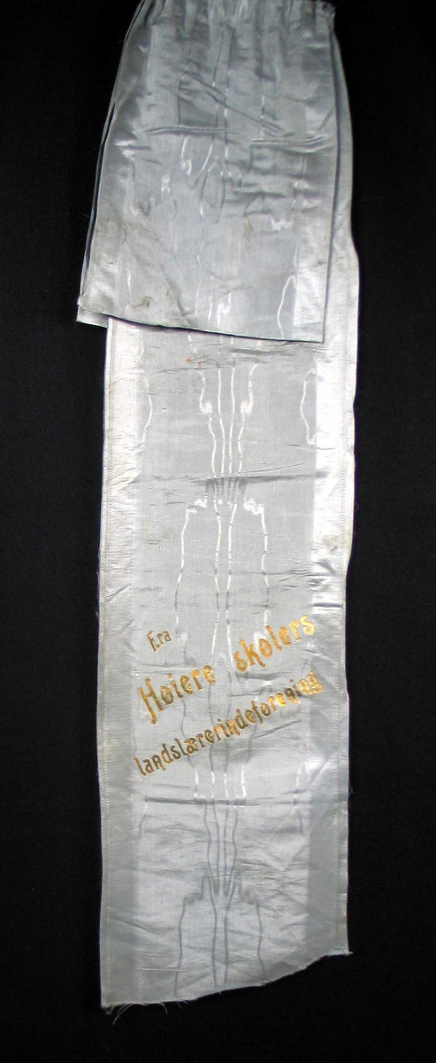 Begravelsessløyfe i grå mønstret silke med tekst i gull.