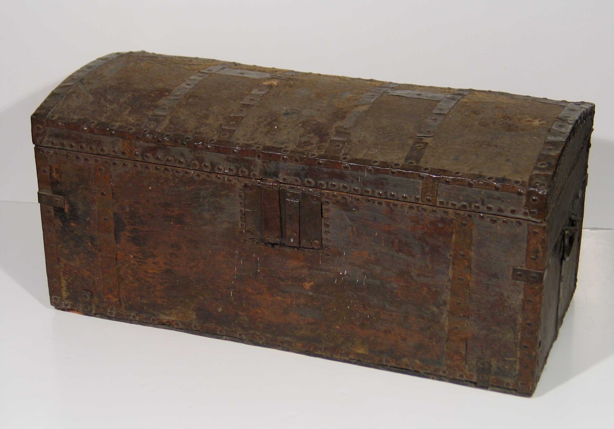 Kiste med hvelvet lokk trukket med kuskinn. Nagler og jernbeslag. Firkantet låsbeslag, komplisert låssystem. To hanker.