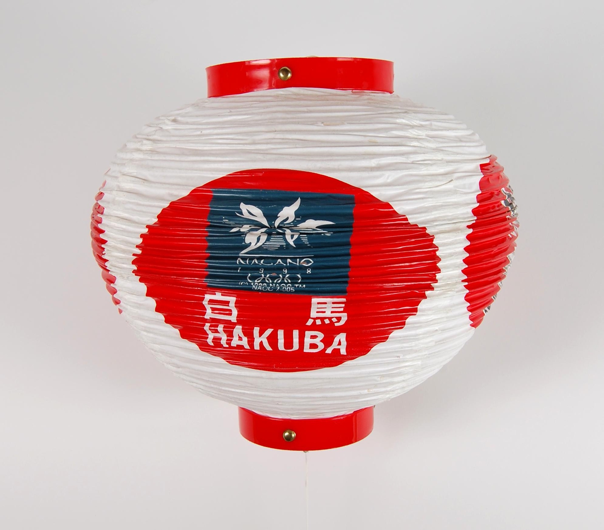 Rund lykt med logo for Paralympics i Nagano i 1998 og de olympiske vinterleker i Nagano i 1998. Lykta kan foldes sammen. Lykta er noe slitt. Den har blant annet noen hull.