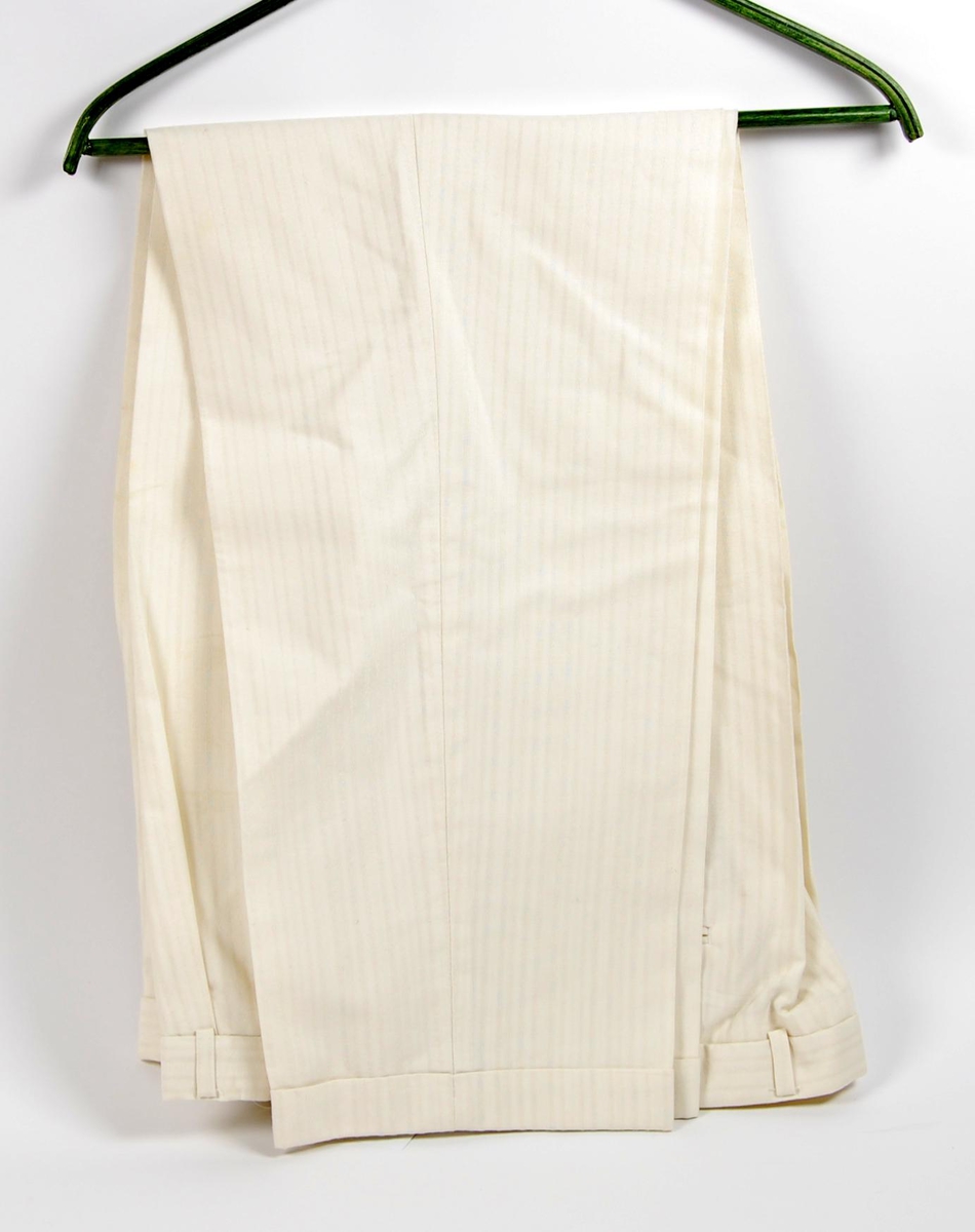 Hvit dress bestående av jakke og bukse. På jakka er det påsydd et merke med de olympiske ringene, norske flagget og innskriften: NORGE. 