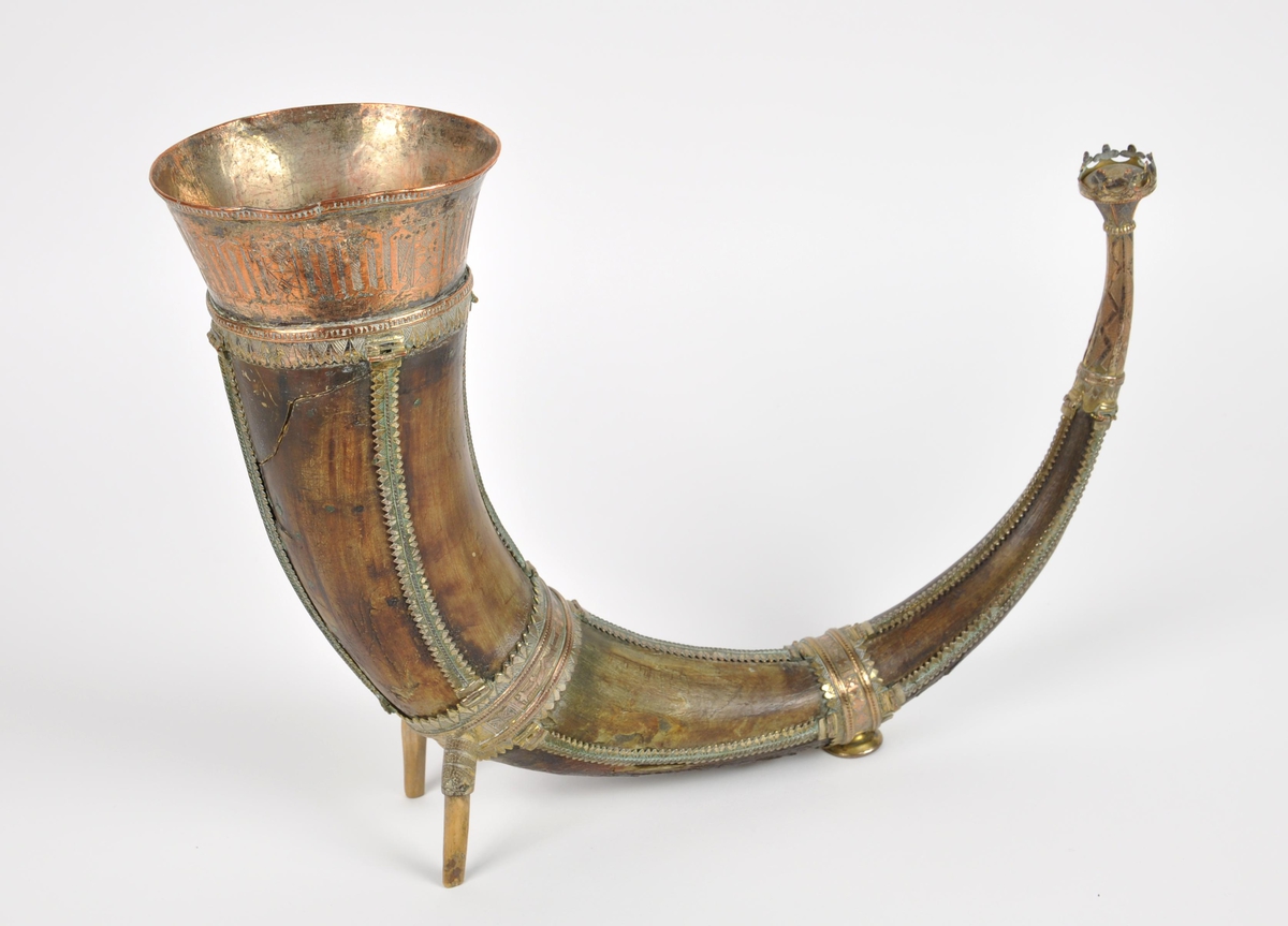 Drikkehorn med metallbeslag rundt kanten, to ringer rundt hornet, et beslag på spissen og smale langsgående beslag. Den største ringen har fester for støttebein. De nåværende beina er ikke de opprinnelige. Beslagene er av forgylt bronse. Krone i spissen. Graverte beslag med geometriske border.