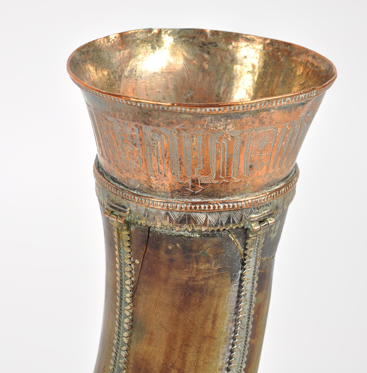 Drikkehorn med metallbeslag rundt kanten, to ringer rundt hornet, et beslag på spissen og smale langsgående beslag. Den største ringen har fester for støttebein. De nåværende beina er ikke de opprinnelige. Beslagene er av forgylt bronse. Krone i spissen. Graverte beslag med geometriske border.