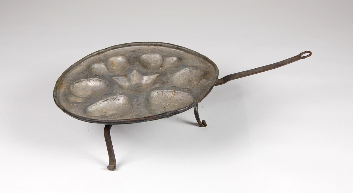 Munkepanne av kobber med fortinnet bunn og seks hjerter med stjerne i midten. Panna har tre bein og håndtak.